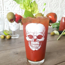 Load image into Gallery viewer, Egads Shop clear 16 ounce tumbler pint drinking glass with white screen print image of skull. Red Bloody Mary drink fills the glass with an olive skewer and celery garnish.